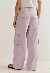 Pantalon cargo lilas avec une coupe large, plusieurs poches et une taille mi-haute. Confectionné dans un tissu léger au toucher lisse.