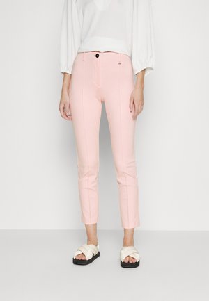 Roze strakke broek met rits, voorzakken en verticale naden. Gedragen met witte platform sandalen met gevlochten banden.