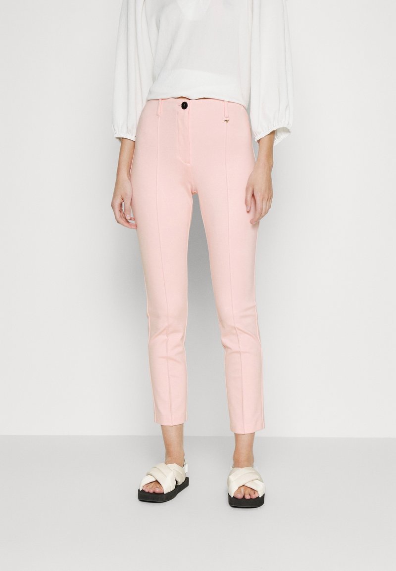 Pink fitted trousers with a zip fly, front pockets, and vertical seams. Worn with white platform sandals featuring braided straps.