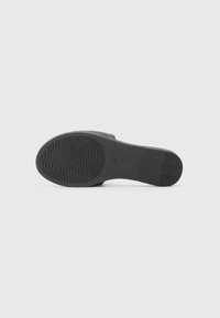 Semelle de chaussure noire avec une surface texturée, présentant un motif ondulé pour l'adhérence, et un marquage de taille numérique, vue par le dessous.