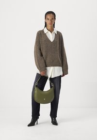 Brun strikket genser med V-hals, over en hvit skjorte med krage. Mørke jeans og svarte ankelstøvler, holder en grønn lærhåndveske.