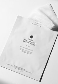 Weiße biologisch abbaubare Verpackung für eine reine Hyaluron-Gesichtsmaske mit schwarzem Text, der die Inhaltsstoffe und Anwendungshinweise beschreibt, teilweise geöffnet.