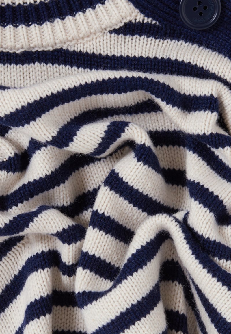 Marineblau und cremefarbener gestreifter Strickstoff, der eine glatte Textur mit einem lockeren, drapierten Aussehen aufweist. Enthält ein Detail mit blauer Knopf.