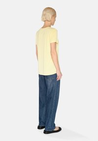 Gele T-shirt met korte mouwen gecombineerd met losse blauwe denim jeans. De T-shirt heeft een ronde hals en de jeans hebben achterzakken.