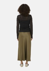 Haut à manches longues noir, texturé, associé à une jupe longue olive. Chaussures comprenant des baskets beige à profil bas avec des accents noirs.