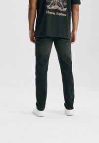 Czarne dżinsy o dopasowanym kroju; mają tylne kieszenie i subtelną teksturę. Połączone z luźną, czarną koszulką z grafiką i białymi tenisówkami.