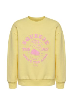 Gul sweatshirt med lyserød tekst "Squeeze the day, serve the game" og grafik af en skrællet appelsin, der afslører en fodbold.