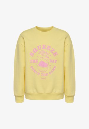 Żółta bluza z różowym napisem „Squeeze the day, serve the game” oraz grafiką obranego pomarańczy, która ukazuje piłkę nożną.