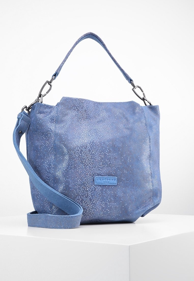 Sac à épaule en cuir bleu avec une surface texturée, doté d'une poignée principale et d'une bandoulière amovible, avec un patch de marque sur le devant.