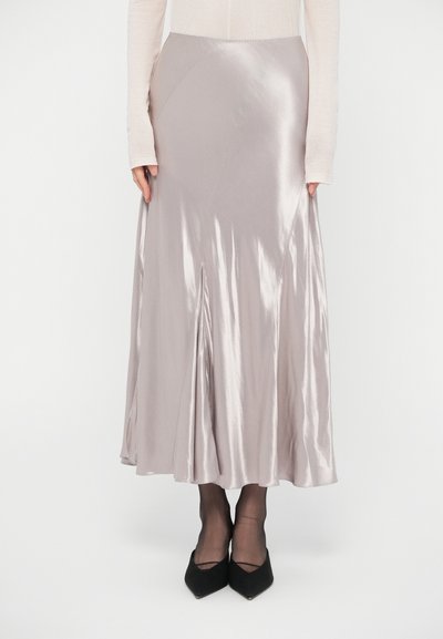 Hellrosa Satinkleidmaxirock mit leichtem Glanz, ungleichmäßigem Saum und einem Schlitz vorne. Kombiniert mit schwarzen spitzen Pumps und transparenten Strumpfhosen.