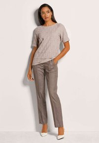 Hellbraunes, strukturiertes Kurzarmoberteil kombiniert mit dunkelbraunen, maßgeschneiderten Hosen und cremefarbenen High-Heels. Einfaches, modernes Design.