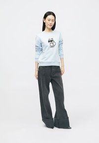 Svetlo modra sweatshirt z grafiko risanega psa, v kombinaciji z ohlapnimi temno sivimi hlačami širokega kroja. Preprost dizajn, sproščen fit.