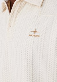 Pullover crema a maglia con design a treccia testurizzata, dotato di colletto pieghevole e logo ricamato in oro sul petto.