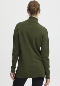 Mörkgrön stickad tröja med hög krage och ribbade ärmslut. Har en avslappnad passform med sidoinsnitt, vilket visar en mjuk textur.
