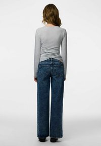 Siv dolg rokav zgornji del z raztrgano hrbtno stranjo, kombiniran z ohlapnimi temno modrimi jeans hlačami. Ima visok pas in klasične zadnje žepe.