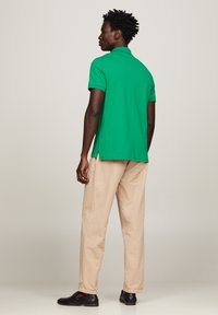 Groene polo met kraag, gecombineerd met lichtbeige broek en zwarte schoenen; heeft zijsplitten aan de onderrand voor extra comfort.
