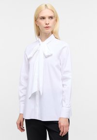 Blusa bianca a maniche lunghe con colletto a fiocco, polsini con bottone e texture liscia, caratterizzata da una vestibilità su misura e senza motivi visibili.