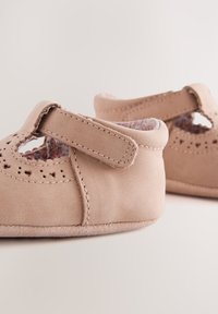 Chaussures bébé beige doux avec des brides Velcro et des détails en forme de cœur découpés, avec doublure en tissu floral à l'intérieur.