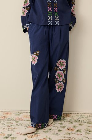 Marineblaue Baumwollkleidung mit weit geschnittenen Hosen und gestickten Blumenmustern in Pink und Grün an Säumen und Ärmeln. Knöpfe vorne.