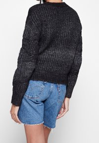 Svart stickad tröja med strukturerade kabelmönster, rund halsringning och ribbat avslut, ihop med ljusblå denimshorts.