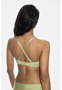 Vihreä rintaliivi, joka on valmistettu sileästä kankaasta ja jossa on ristikkäiset säätöremmit sekä koukku kiinnitys selässä.