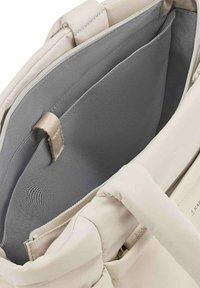 Sac fourre-tout matelassé beige avec un compartiment intérieur en tissu gris et une petite boucle en tissu beige à l'intérieur.