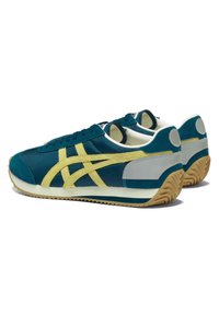 Teal suede sneakers with yellow stripes, contrasting grey accents, and a textured rubber sole. Vintage design with lace-up closure.