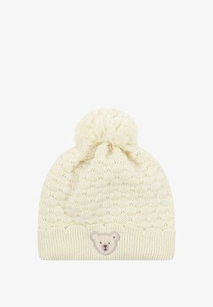 Knitted cream beanie with a textured pattern, rounded top, and a fluffy pom-pom. Features a bear face patch on the front.