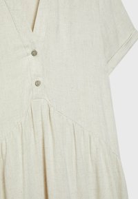 Robe en lin beige à manches courtes, encolure en V, deux boutons en bois, et détail de tissu froncé sous la taille.