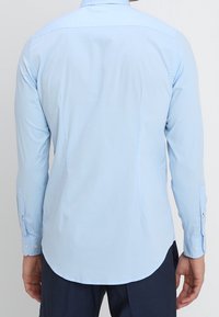Camisa de manga larga azul claro hecha de una tela suave, con un dobladillo curvado, puños con botones y un diseño de cuello estándar.