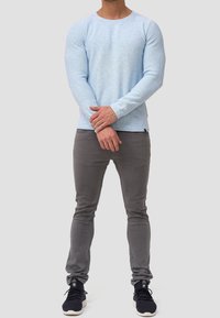 Chemise bleu clair à manches longues en tissu texturé, associée à un pantalon gris ajusté et des baskets noires, avec un col rond simple.