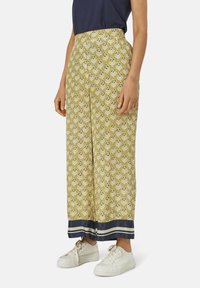 Pantaloni a gamba larga gialli con motivo floreale e orlo a righe navy, abbinati a sneaker bianche. Tessuto leggero, vestibilità ampia.