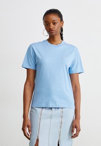 T-shirt di cotone azzurro chiaro con maniche corte, collo rotondo e piccolo logo sul petto. Design semplice e casual con una texture liscia.