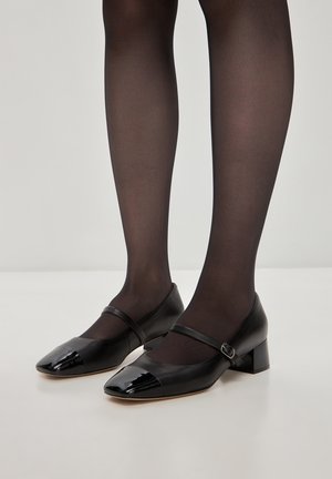 Zapatos Mary Jane de charol negro con punta redonda, tacón bajo y bloque, y una correa ajustable en la parte superior. Con detalles de punteras brillantes.