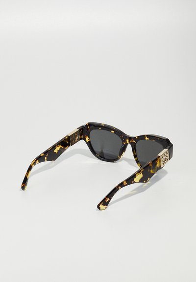 Occhiali da sole tartarugati con una montatura spessa, lenti scure e aste decorate con accenti dorati e un motivo geometrico.