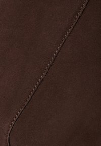 Brown suede material with a smooth texture, featuring a prominent seam detail. The surface appears soft and slightly brushed.