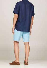 Navy short-sleeve linen shirt paired with light blue shorts. Casual brown boat shoes complete the outfit.