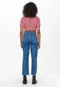 Rotes, floral bedrucktes Crop-Top mit kurzen Ärmeln, kombiniert mit hochgeschnittenen blauen Jeans. Die Jeans haben einen ausgewaschenen Look und einen rohen Saum. Schwarze Plattformstiefel.