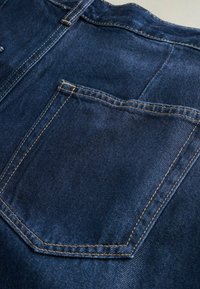 Donkerblauwe denimstof heeft een rechthoekige achterzak met contrasterende stiksels en een gladde textuur, wat de duurzaamheid en het ontwerp benadrukt.
