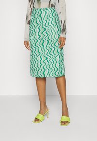 Zelená midi sukně s bílým vlnitým vzorem, lehký materiál a hladká textura. Vytvořeno s odpovídajícími světlými zelenými sandály na podpatku.
