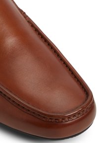 Zapato de cuero marrón con un acabado suave, punta redondeada y costura visible a lo largo del borde. La suela es ligeramente curvada.
