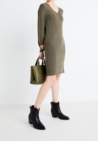 Abito a coste verde oliva con scollo a V e maniche lunghe; stivaletti neri in pelle con punta affusolata e tacco a blocco; borsa verde.