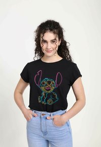 Černé tričko s barevným neonovým obrysem Stitche, krátké rukávy a volný střih. Spárováno se světle modrými džíny s vysokým pasem.