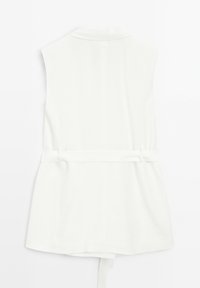 Valkoinen hihaton vaatekappale, jossa on kauluksellinen pääntie ja sidottava vyötärönauha. Sileä pinta, levenevä helma ja pelkistetty muotoilu.