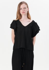 Black short-sleeve top with a V-neckline, featuring textured fabric with wavy patterns and layered ruffles along the sleeves.