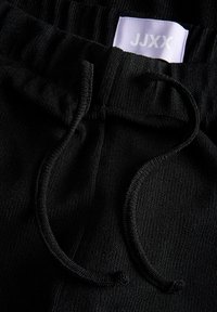 Pantalon en tricot noir avec taille élastique et cordon, avec une étiquette blanche portant le texte « JJXX ».