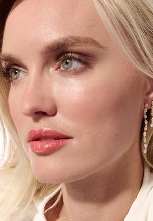 Klare krystal dråbeøreringe med delikate kæder med en poleret finish, suppleret af en glat, lys hudtone og en blød læbefarve.