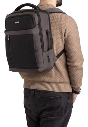 Zaino nero e grigio realizzato in tessuto resistente, dotato di una tasca frontale con zip, schienale imbottito e spallacci regolabili. Finitura liscia con dettaglio del logo.