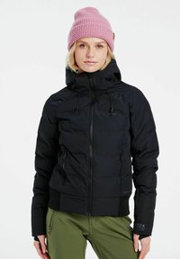 Schwarze Daunenjacke mit Reißverschluss und Kapuze, mit seitlichen Taschen und gerippten Bündchen. Kombiniert mit olivgrünen Hosen und einer hellrosa Strickmütze.