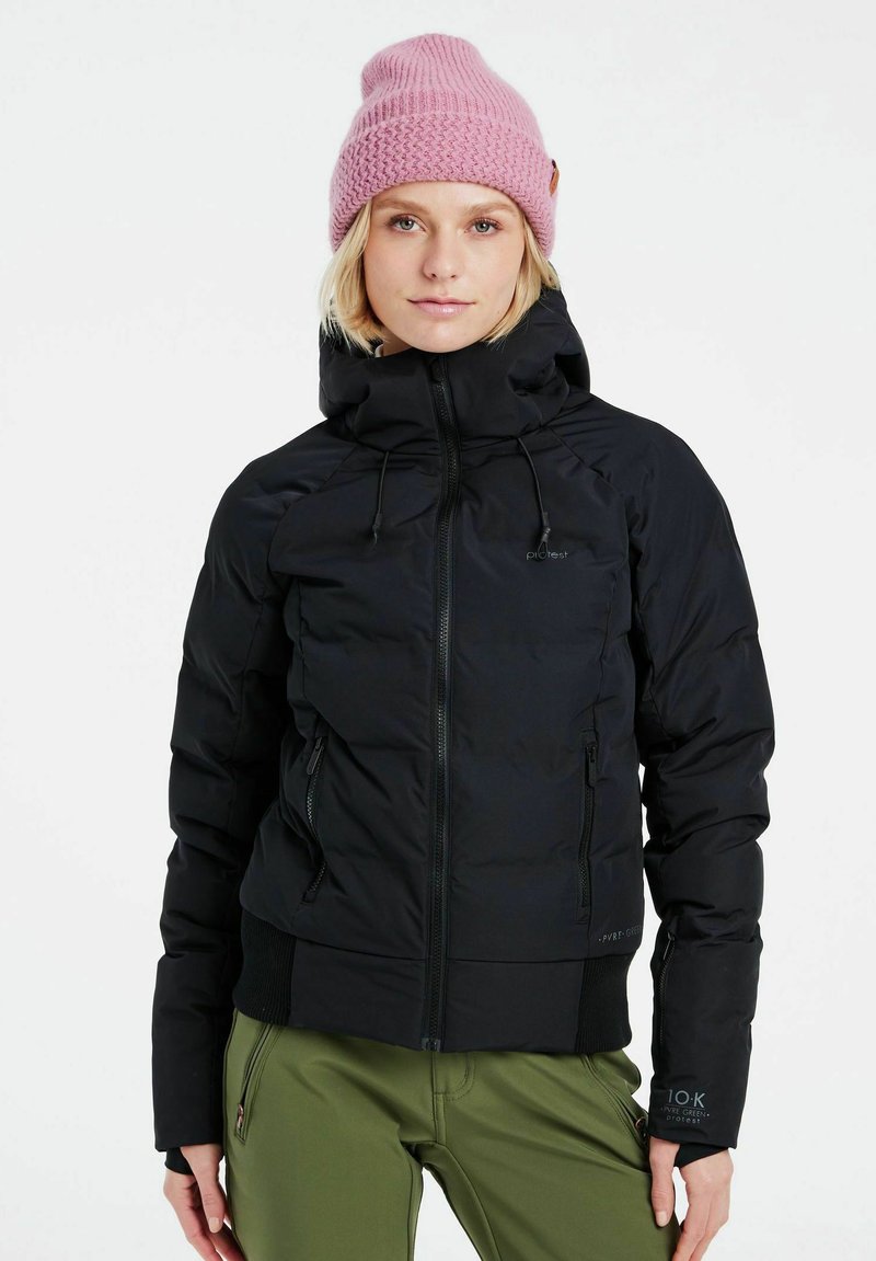 Schwarze Daunenjacke mit Reißverschluss und Kapuze, mit seitlichen Taschen und gerippten Bündchen. Kombiniert mit olivgrünen Hosen und einer hellrosa Strickmütze.